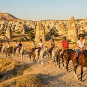 Tourists enjoying a sunset horseback riding tour in Cappadocia, Turkey, amidst scenic fairy chimney rock formations.