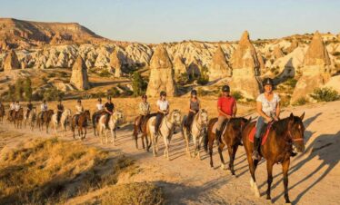 Tourists enjoying a sunset horseback riding tour in Cappadocia, Turkey, amidst scenic fairy chimney rock formations.