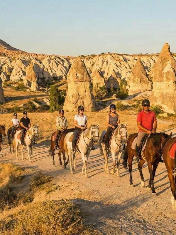 Tourists enjoying a sunset horseback riding tour in Cappadocia, Turkey, amidst scenic fairy chimney rock formations.