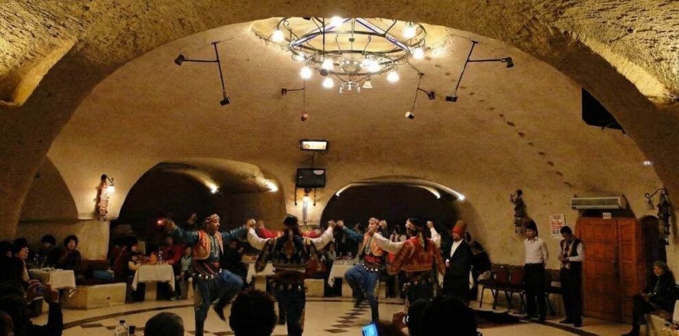 Traditional folk dancers perform at a Cappadocia Turkish Night Show in a cave restaurant venue with a seated audience