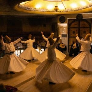 Whirling Dervishes performing traditional Sema ceremony in a Cappadocia cave venue wearing white robes and tall hats.