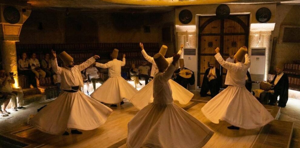 Whirling Dervishes performing traditional Sema ceremony in a Cappadocia cave venue wearing white robes and tall hats.