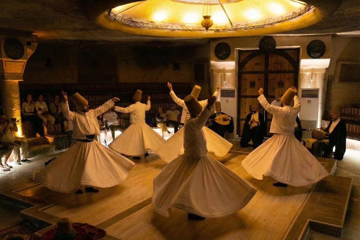 Whirling Dervishes performing traditional Sema ceremony in a Cappadocia cave venue wearing white robes and tall hats.