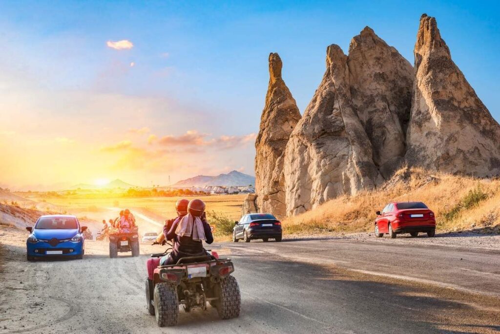 Travelers on ATVs ride past unique Cappadocia rock formations at sunset on a scenic adventure route.