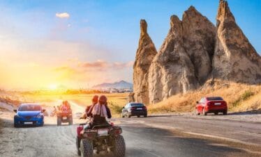 Travelers on ATVs ride past unique Cappadocia rock formations at sunset on a scenic adventure route.