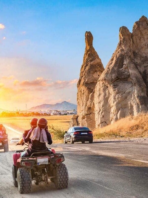 Travelers on ATVs ride past unique Cappadocia rock formations at sunset on a scenic adventure route.