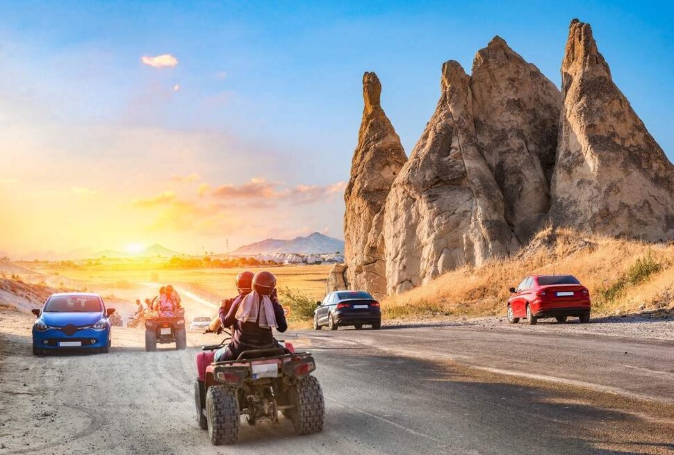 Travelers on ATVs ride past unique Cappadocia rock formations at sunset on a scenic adventure route.