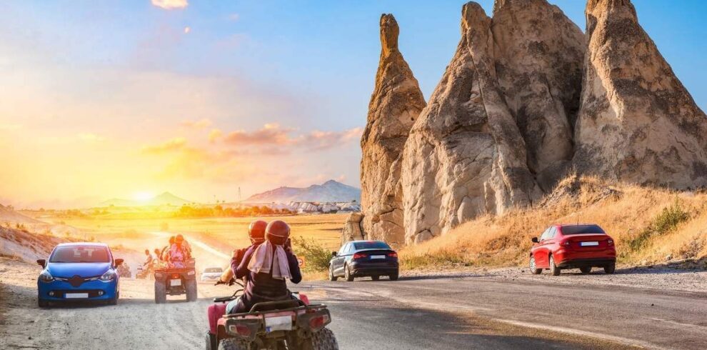 Travelers on ATVs ride past unique Cappadocia rock formations at sunset on a scenic adventure route.