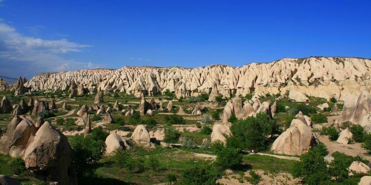 Unique cone-shaped rock formations and lush greenery in Belisirma Village, Cappadocia, under a vibrant blue sky.