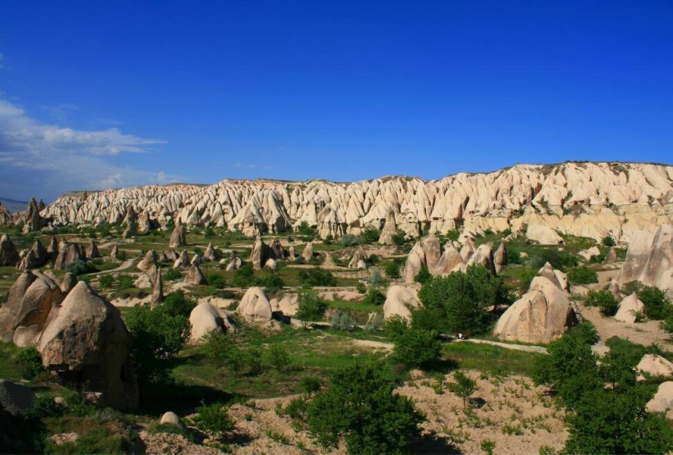 Unique cone-shaped rock formations and lush greenery in Belisirma Village, Cappadocia, under a vibrant blue sky.
