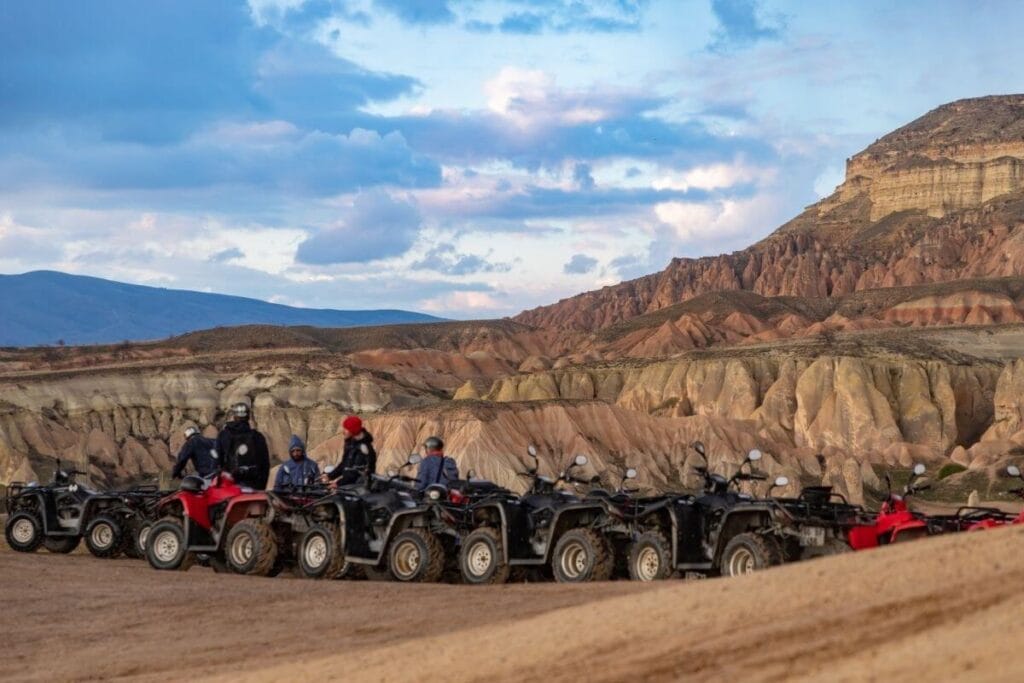Group of travelers on ATVs exploring Cappadocia’s rocky valleys under a vibrant evening sky.