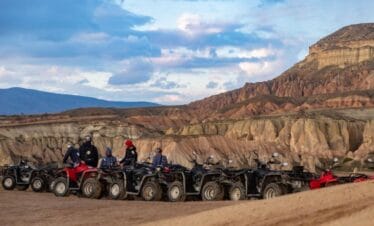 Group of travelers on ATVs exploring Cappadocia’s rocky valleys under a vibrant evening sky.