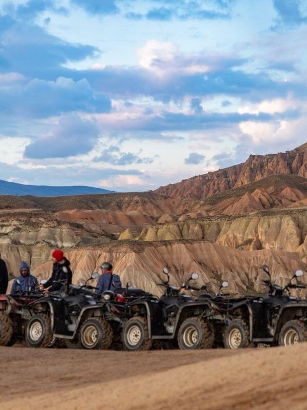 Group of travelers on ATVs exploring Cappadocia’s rocky valleys under a vibrant evening sky.