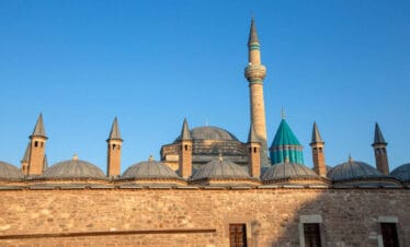 Mevlana Museum in Konya, Turkey with turquoise dome and historic minaret under clear blue sky, a key Sufi heritage site.