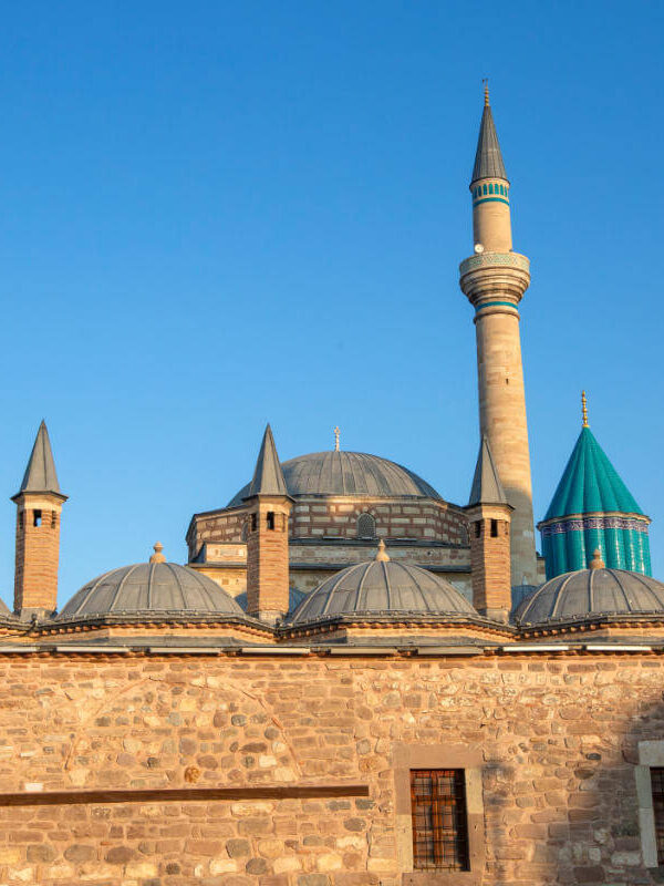 Mevlana Museum in Konya, Turkey with turquoise dome and historic minaret under clear blue sky, a key Sufi heritage site.