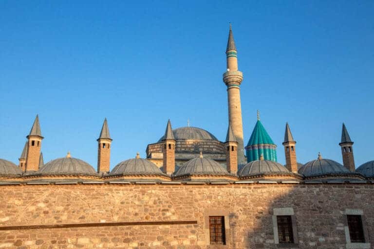 Mevlana Museum in Konya, Turkey with turquoise dome and historic minaret under clear blue sky, a key Sufi heritage site.
