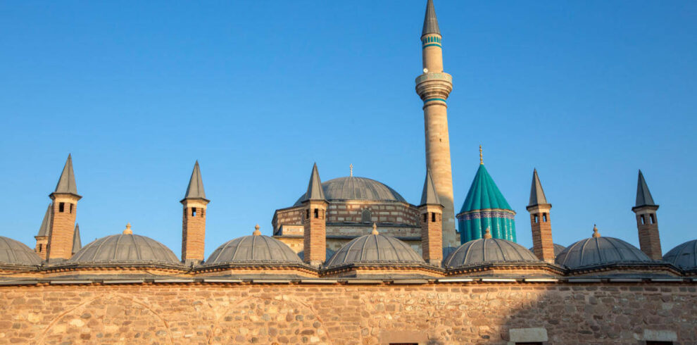 Mevlana Museum in Konya, Turkey with turquoise dome and historic minaret under clear blue sky, a key Sufi heritage site.