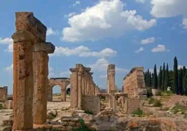 Remains of stone columns and arches from ancient Roman ruins in Hierapolis, Turkey, under a bright, cloudy sky.