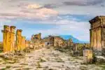 Ruins of the Byzantine Gate in Hierapolis, Turkey, with stone columns and distant mountains under a colorful evening sky.