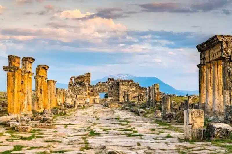 Ruins of the Byzantine Gate in Hierapolis, Turkey, with stone columns and distant mountains under a colorful evening sky.