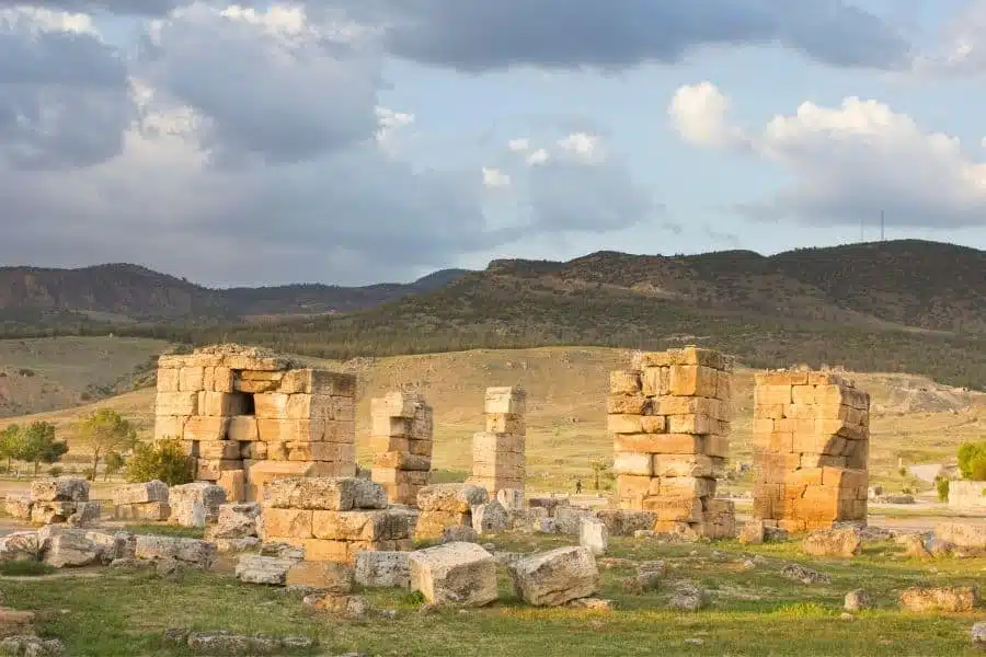 Stone remnants of the ancient cathedral at Hierapolis, Turkey, with mountainous scenery under a cloudy sky.