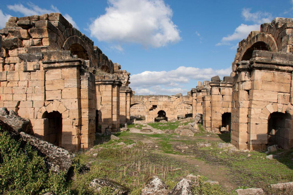 Ancient Roman bath ruins with arched stone entrances and weathered walls under a bright blue sky.