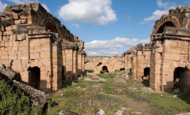 Ancient Roman bath ruins with arched stone entrances and weathered walls under a bright blue sky.