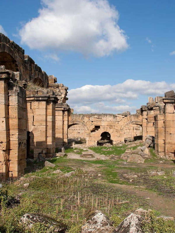 Ancient Roman bath ruins with arched stone entrances and weathered walls under a bright blue sky.