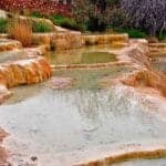 Iron-rich travertine terraces at Karahayit Red Springs with warm thermal pools and natural vegetation.