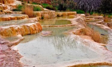 Iron-rich travertine terraces at Karahayit Red Springs with warm thermal pools and natural vegetation.