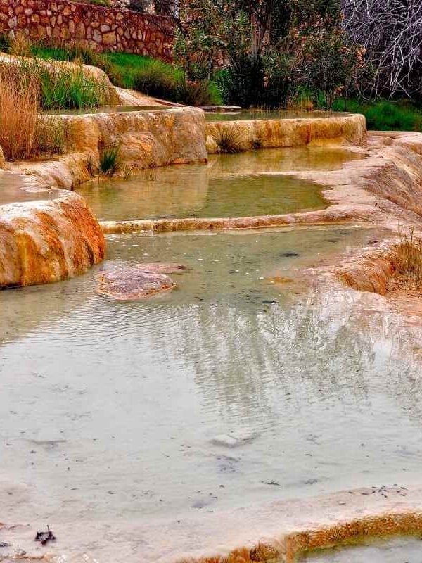 Iron-rich travertine terraces at Karahayit Red Springs with warm thermal pools and natural vegetation.