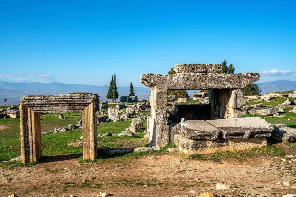 Ancient stone tombs and ruins in the necropolis of Hierapolis, Denizli, under a clear blue sky with distant mountains.