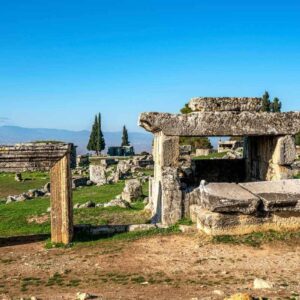 Ancient stone tombs and ruins in the necropolis of Hierapolis, Denizli, under a clear blue sky with distant mountains.