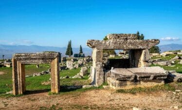 Ancient stone tombs and ruins in the necropolis of Hierapolis, Denizli, under a clear blue sky with distant mountains.