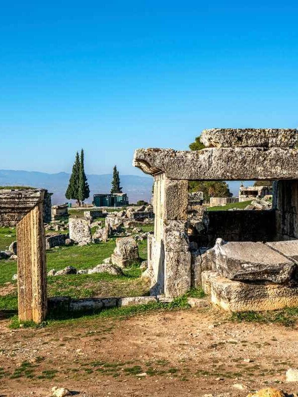Ancient stone tombs and ruins in the necropolis of Hierapolis, Denizli, under a clear blue sky with distant mountains.