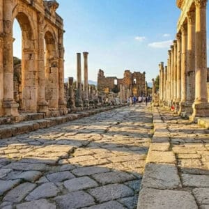 Ancient Frontinus Street in Hierapolis, Pamukkale, featuring stone columns, paved road, and historic ruins under a blue sky.
