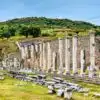 Stone columns and ruins of the Asclepieion of Pergamon set against a green hillside under a clear sky.