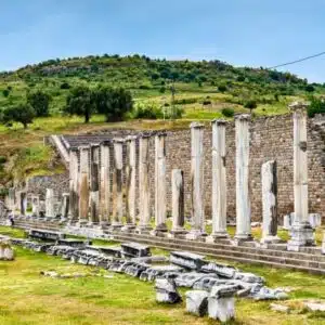 Stone columns and ruins of the Asclepieion of Pergamon set against a green hillside under a clear sky.