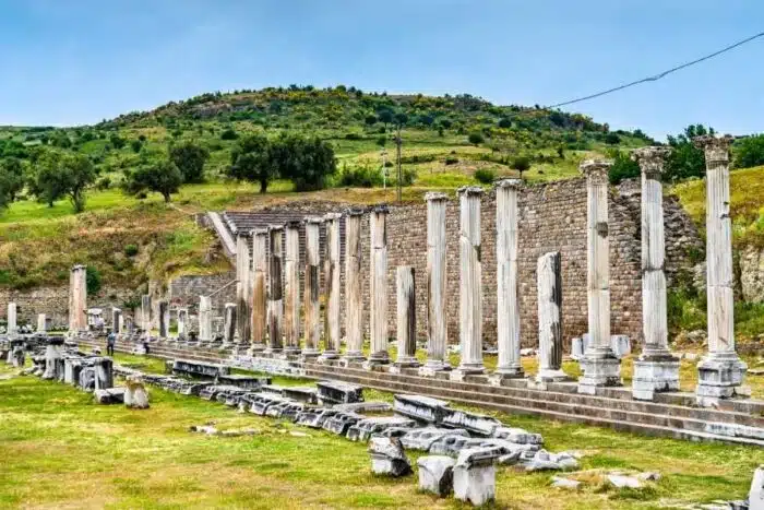 Stone columns and ruins of the Asclepieion of Pergamon set against a green hillside under a clear sky.