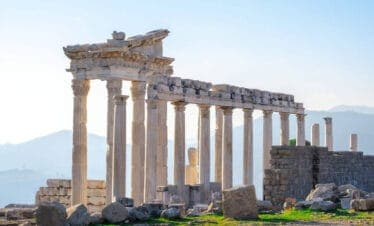 Marble columns and ancient ruins of the Temple of Trajan at Pergamon in Bergama, Turkey, with a scenic mountain backdrop.