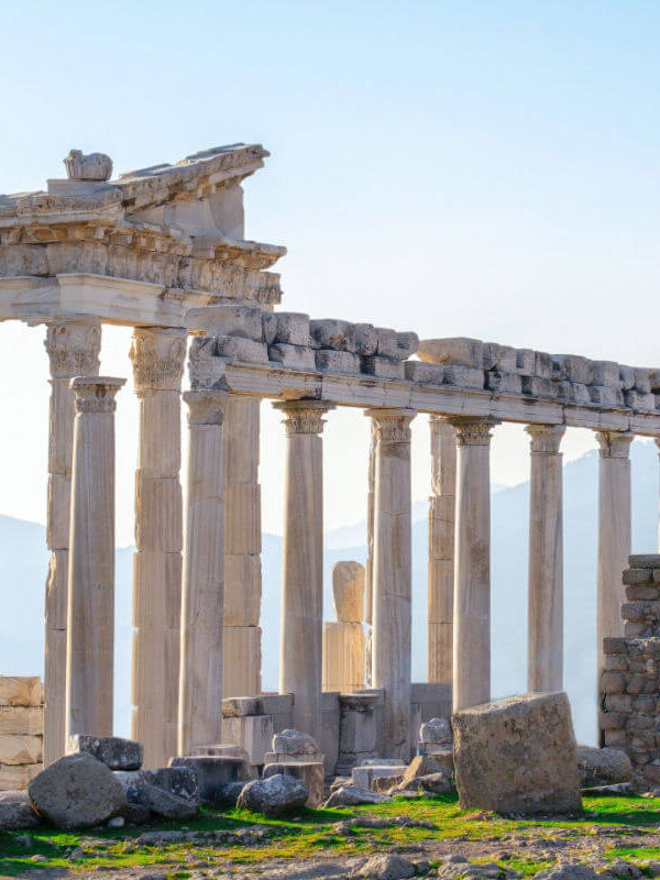 Marble columns and ancient ruins of the Temple of Trajan at Pergamon in Bergama, Turkey, with a scenic mountain backdrop.