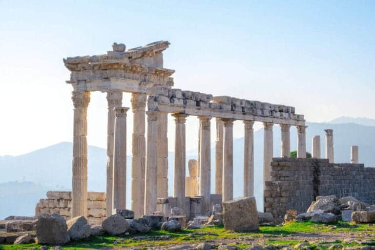 Marble columns and ancient ruins of the Temple of Trajan at Pergamon in Bergama, Turkey, with a scenic mountain backdrop.