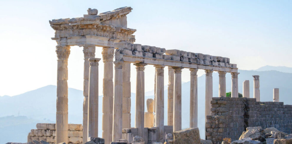 Marble columns and ancient ruins of the Temple of Trajan at Pergamon in Bergama, Turkey, with a scenic mountain backdrop.