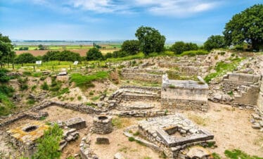 Stone walls and excavated ruins of ancient Troy in Çanakkale, surrounded by dry grass and open skies.