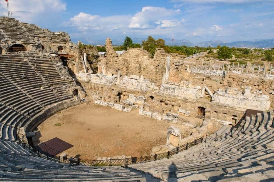 Ancient Roman theatre in Side, Antalya, featuring stone seating and weathered ruins under a bright sky.