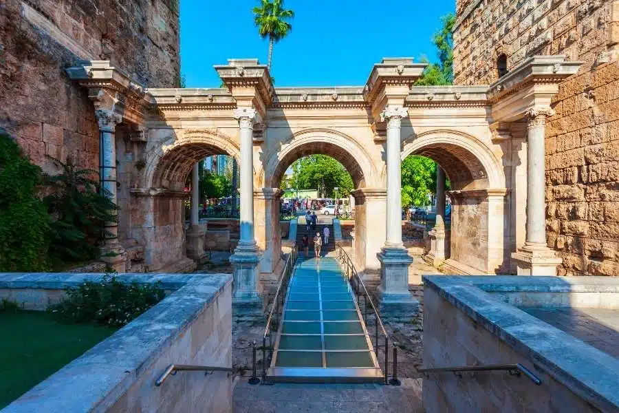 Historic Hadrian’s Gate in Antalya, featuring Roman arches, stone columns, and a modern glass walkway under bright daylight.