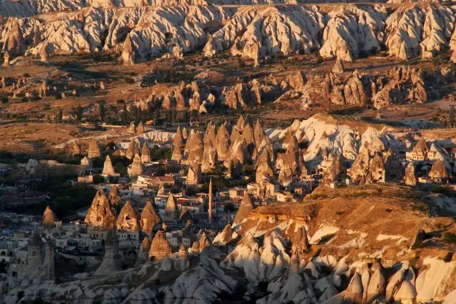 Aerial view of Esentepe, Cappadocia, showcasing rock formations, cave houses, and a village under warm sunset light.