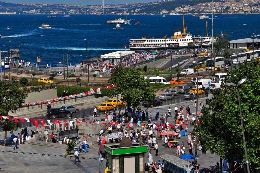 Busy street scene in Eminönü, Istanbul, with crowds, taxis, and ferries in the Bosphorus, decorated with Turkish flags.