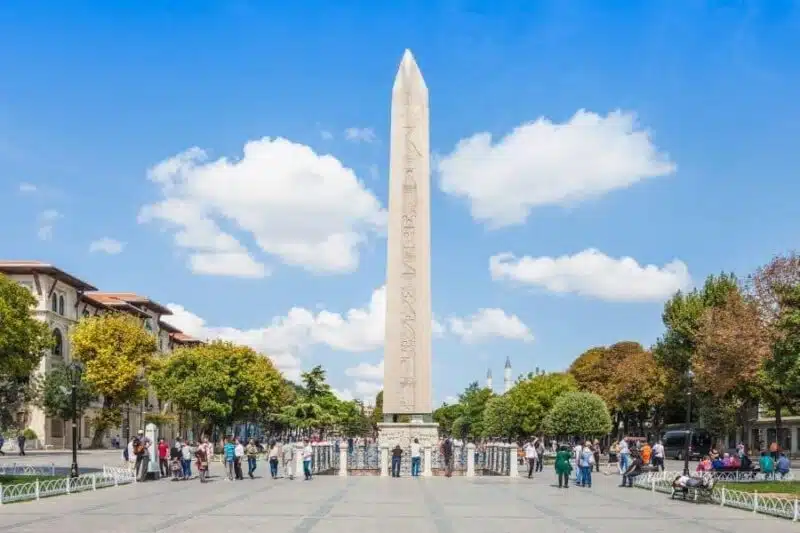 The Obelisk of Theodosius in Istanbul’s Hippodrome Square with tourists gathered around on a bright, sunny day.