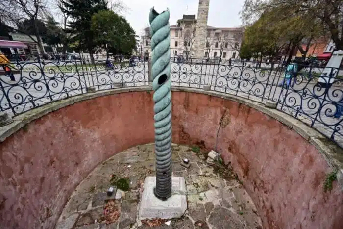 The Serpent Column in Istanbul’s Hippodrome, featuring a twisted bronze design in a circular pit with a surrounding metal fence.